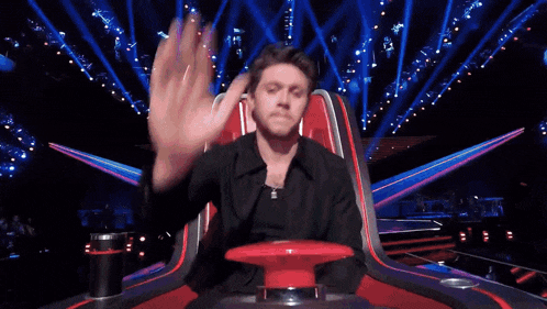 a man is sitting in a red chair on a stage with a lot of lights