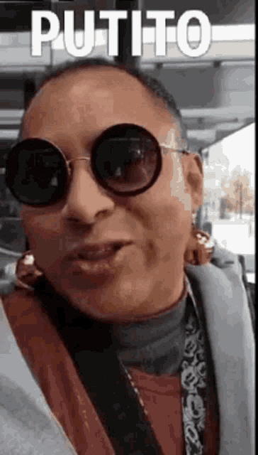 a man wearing sunglasses and earrings is making a funny face and says putito .