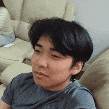 a young man in a grey shirt sits on a couch with his eyes closed