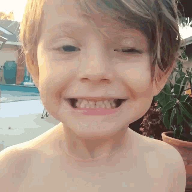 a young boy without a shirt is smiling and looking at the camera
