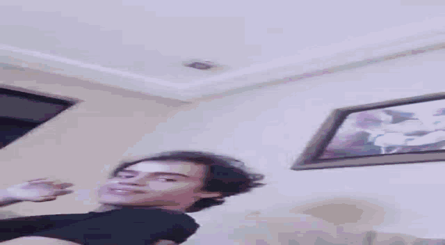a man in a black shirt is standing in a room with a picture on the wall .