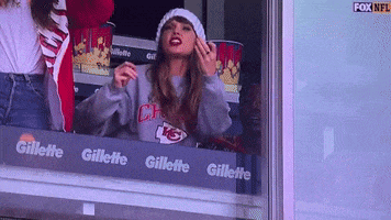 a woman in a gillette sweatshirt looks out a window at a football game