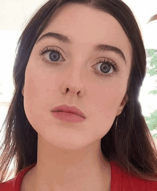 a close up of a woman 's face with blue eyes and a red shirt