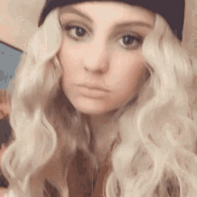 a woman with blonde hair and a black hat is making a face .