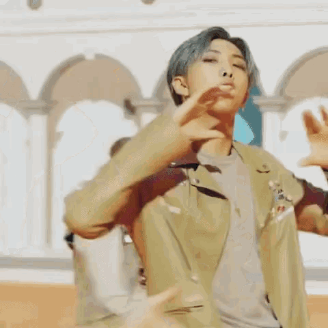 a man with blue hair is dancing in front of a building while wearing a jacket and a gray shirt .