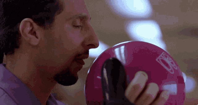 a man in a purple shirt holds a pink bowling ball with the letter d on it