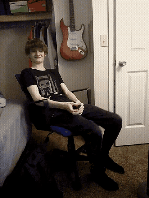 a young man is sitting in a chair in front of a guitar