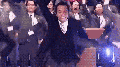 a man in a suit and tie is standing in front of a crowd of people with his arms in the air .