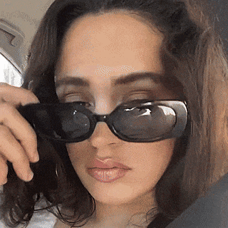 a woman wearing sunglasses is taking a selfie in a car .