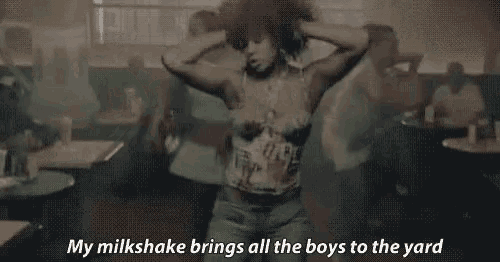 a woman is dancing in a room with a crowd of people and a milkshake .