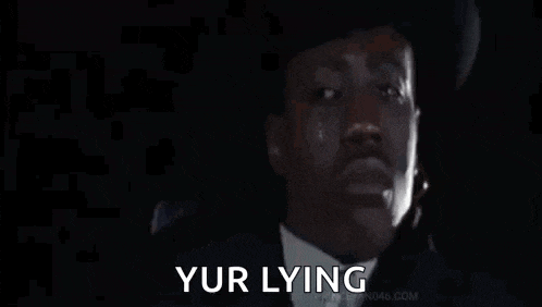 a man in a suit and hat is pointing a gun at the camera and saying `` your lying '' .