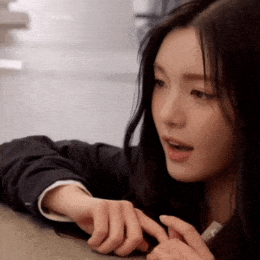a woman with long black hair is laying on a table with her hand on her face