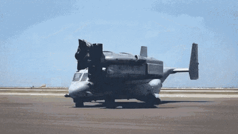 a military helicopter is sitting on a runway with its landing gear down .