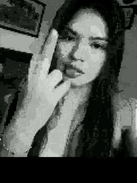 a black and white photo of a woman with long hair making a peace sign .