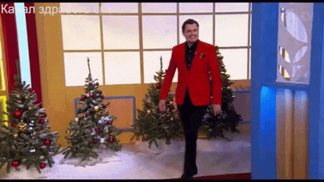a man in a red jacket stands in front of a christmas tree