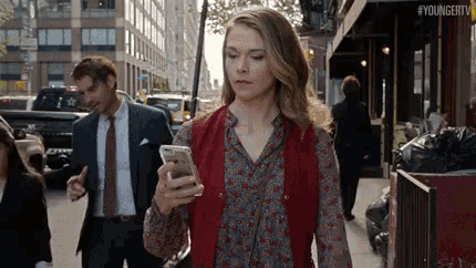 a woman is walking down a street while looking at her phone .