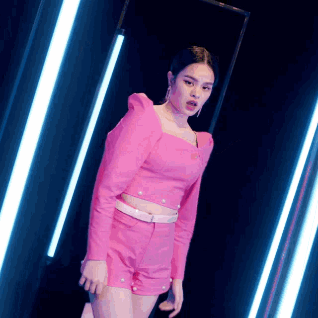 a woman in a pink crop top and shorts stands in front of a row of lights