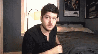 a man with a beard is sitting on a bed in a bedroom with a poster of star wars on the wall .