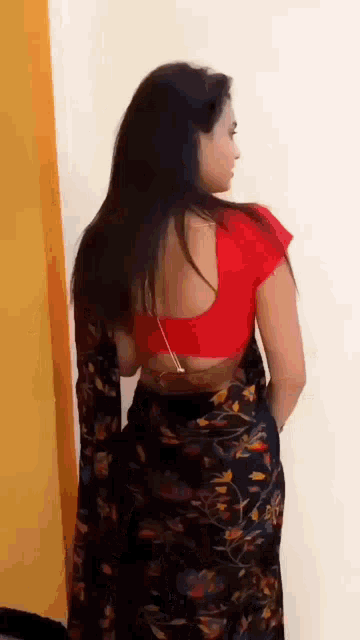 a woman wearing a red blouse and a black floral saree