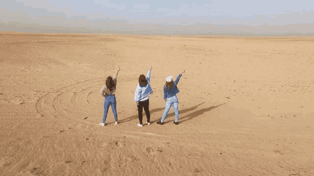 three women are standing in the middle of a desert with their arms in the air