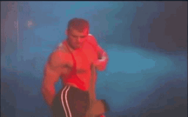 a man in a red tank top and black shorts is standing in front of a blue background .