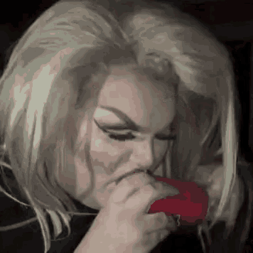 a woman in a wig is holding a red object in her hand .