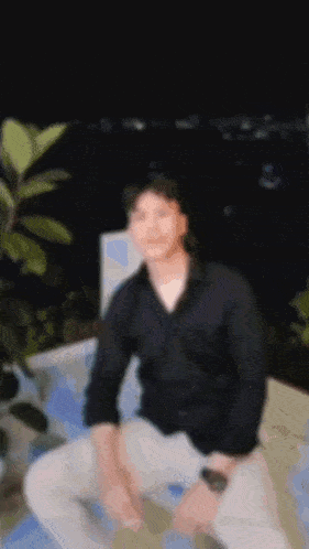 a blurry picture of a man in a black shirt sitting on a ledge .