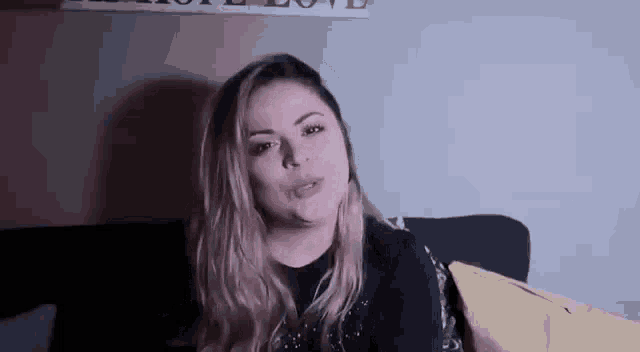 a woman is sitting on a couch in a dark room talking to the camera .
