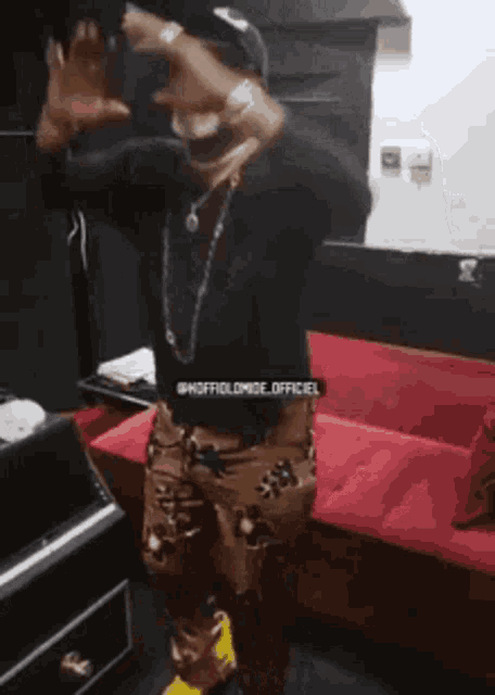 a man in a black shirt and brown pants is standing in front of a red couch and making a funny face .