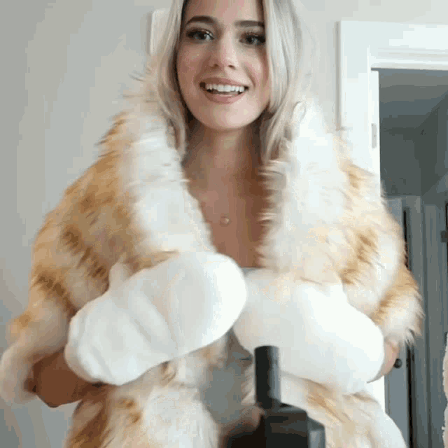 a woman wearing a fur coat and white gloves is smiling