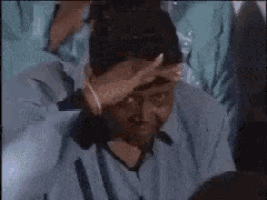 a man in a blue shirt is covering his face with his hand