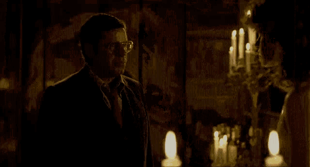 a woman in a bra is standing in front of a man in a dark room with candles .