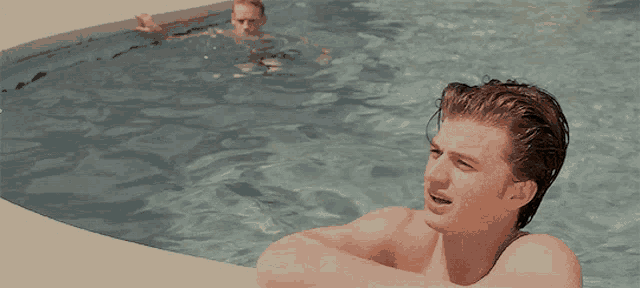 a man sits in a swimming pool watching another man swim in the water