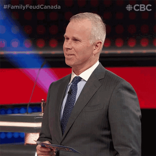 a man in a suit and tie is standing in front of a microphone with the hashtag #familyfeudcanada
