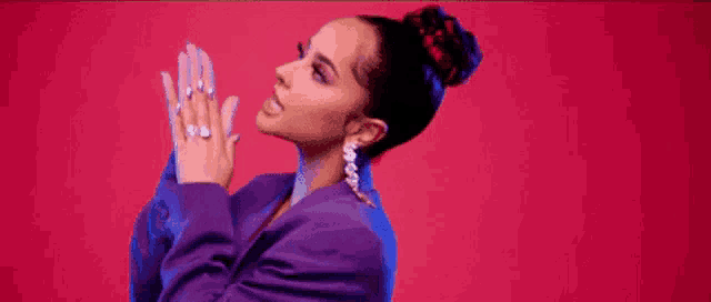 a woman in a purple jacket is praying with her hands together .