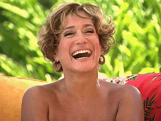 a shirtless woman is laughing while sitting on a couch