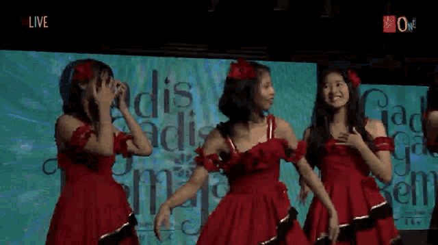 three girls in red dresses are dancing in front of a live screen