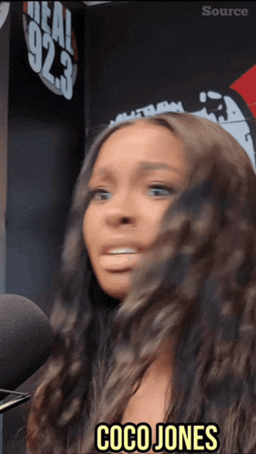 a woman says coco jones in front of a 92.3 sign