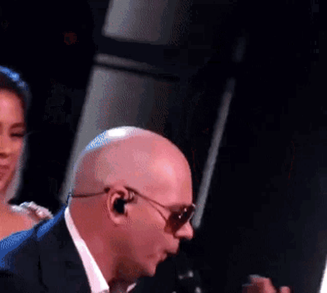 a bald man singing into a microphone with sunglasses on