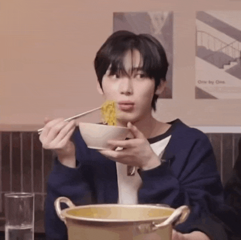a young man is eating a bowl of noodles with chopsticks .