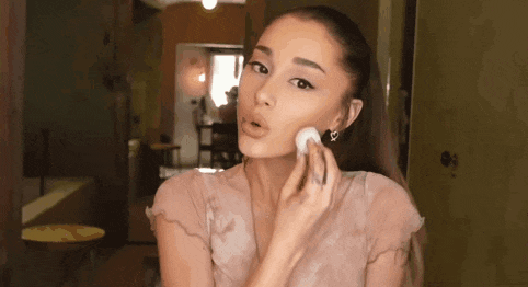 ariana grande is applying makeup to her face with a brush .