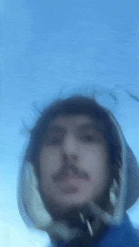 a blurry picture of a man wearing a helmet and a hood against a blue sky .