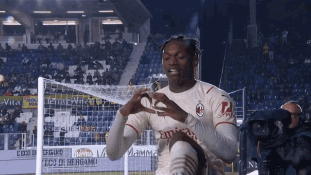 a soccer player wearing a jersey that says emirates makes a heart shape with his hands