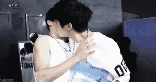 two men are kissing in front of a mirror in a locker room .