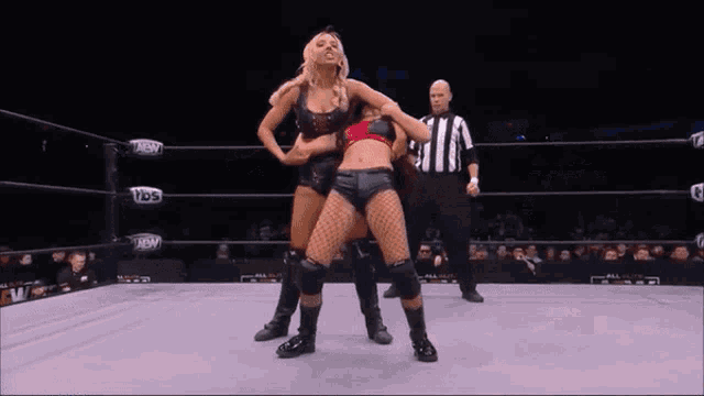 two women are wrestling in a wrestling ring while a referee watches .