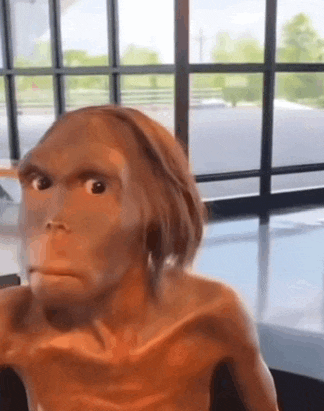 a close up of a statue of a monkey looking at the camera in front of a window .
