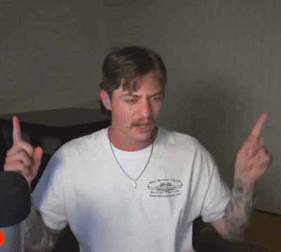 a man wearing a white t-shirt with a necklace around his neck is giving the middle finger