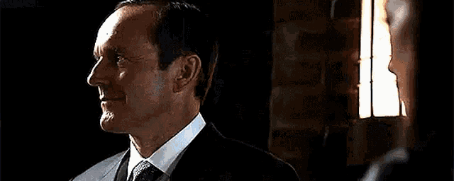 a woman in a black suit is standing next to a man in a dark room and looking at the camera .