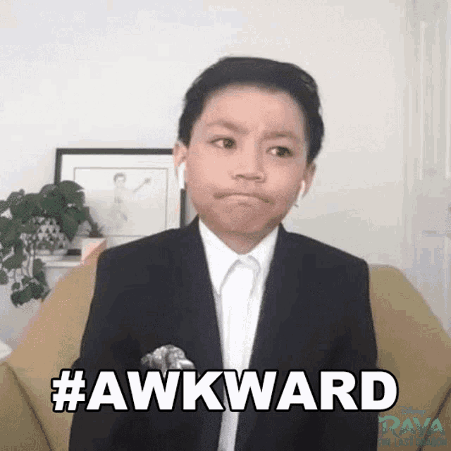a young boy in a suit and tie is sitting in a chair and making a funny face while wearing headphones .