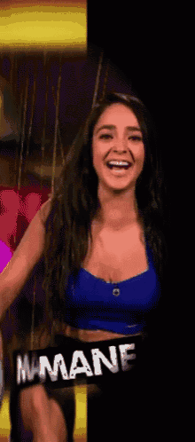 a woman in a blue crop top is smiling and wearing a sign that says mamane